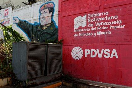 El logotipo de la petrolera estatal venezolana PDVSA se ve junto a un mural que representa al difunto presidente de Venezuela, Hugo Chávez, en una estación de servicio en Caracas, Venezuela, 2 de marzo de 2017. (Reuters/Carlos Garcia Rawlins/archivo)