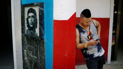 Un joven cubano revisa su teléfono en un punto de acceso a internet junto a una foto del fallecido héroe revolucionario Ernesto "Che" Guevara en La Habana, Cuba. 10 de agosto de 2018. REUTERS/Tomas Bravo