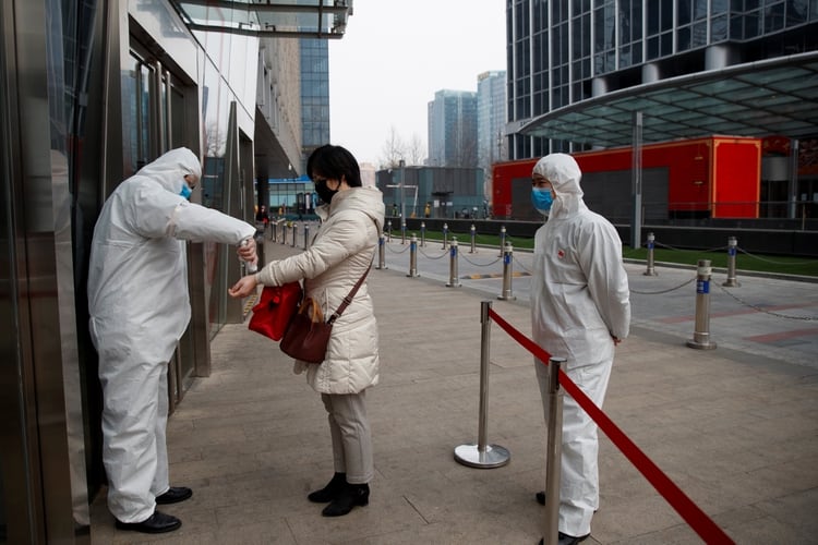 Un trabajador comprueba la temperatura de una mujer al entrar a un edificio de oficinas en el Distrito Central de Negocios de Beijing el 24 de febrero de 2020, mientras el país se ve afectado por un brote del novedoso coronavirus (REUTERS/Thomas Peter)