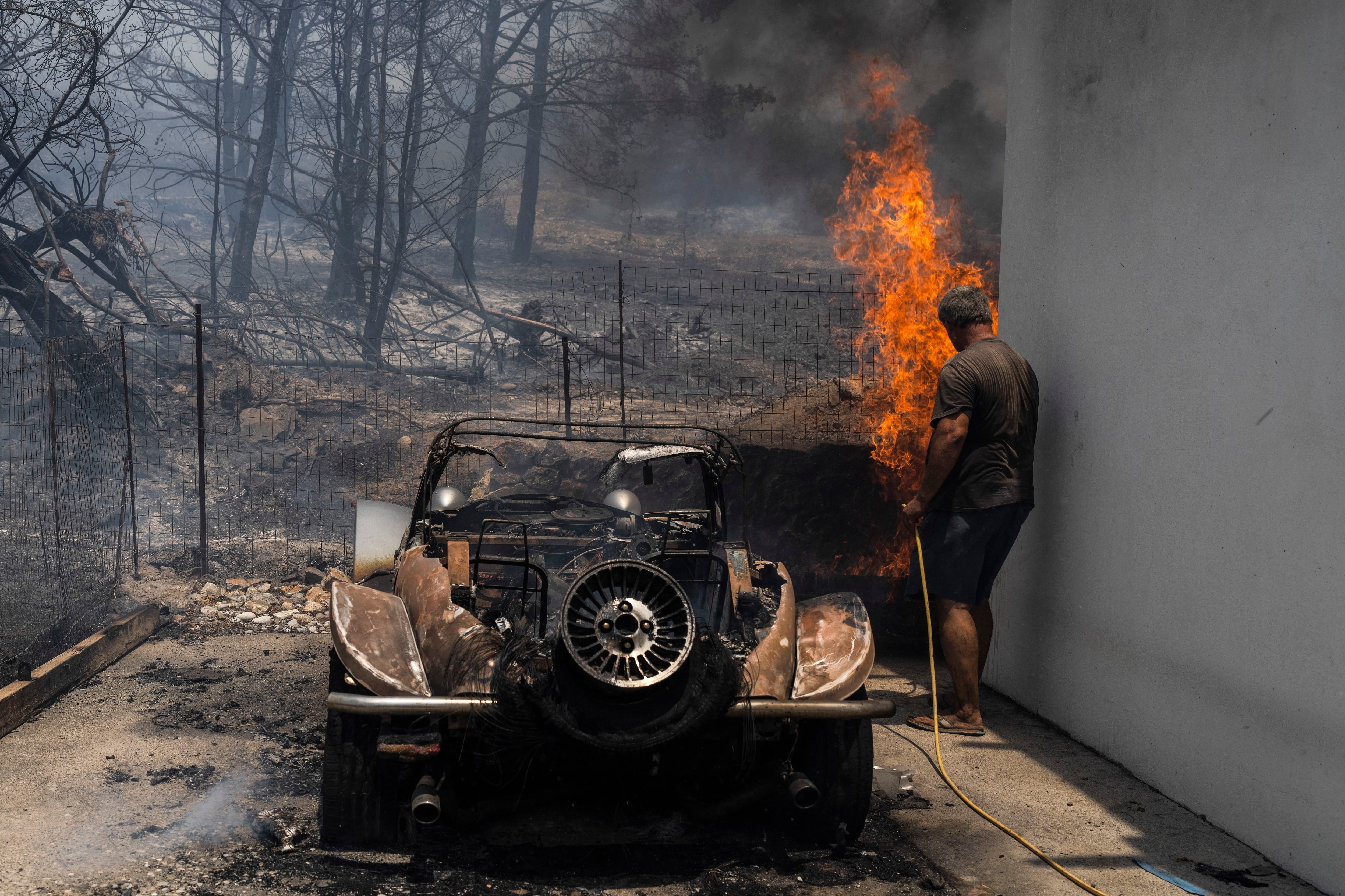Un residente trata de apagar un fuego en el patio de una casa, junto a un auto calcinado. (AP Foto/Petros Giannakouris)