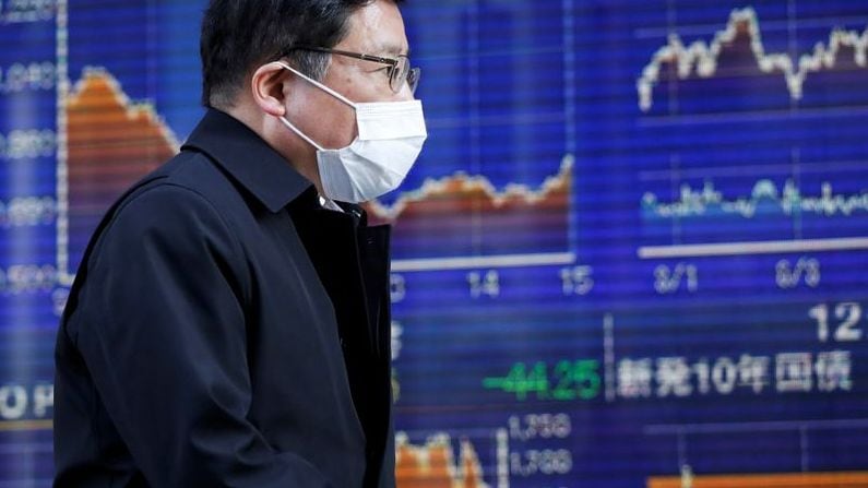 Foto de archivo de un hombre con una máscara protectora para el coronavirus caminando delante de una pantalla que mueestra los movimientos del índice Nikkei en Tokio. 
Mar 6, 2020. REUTERS/Issei Kato