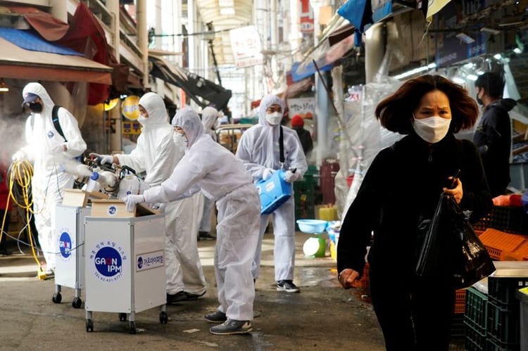 Una mujer que usa una mascarilla para evitar contraer el coronavirus reacciona cuando los empleados de una empresa de servicios de desinfección desinfectan un mercado tradicional en Seúl, Corea del Sur. REUTERS/Kim Hong-Ji.