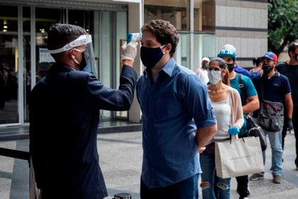 Un guardia toma la temperatura a personas que hacen fila para ingresar a un centro comercial, en Caracas (Venezuela). EFE/Rayner  