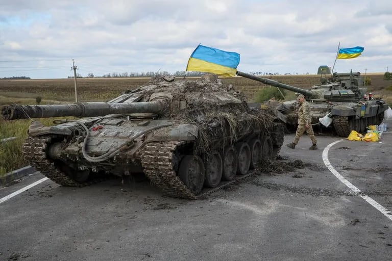 Un militar ucraniano camina cerca de tanques rusos capturados con banderas ucranianas puestas sobre ellos, mientras con 
