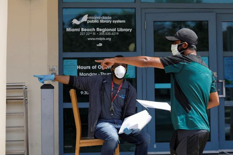 Un hombre conversa con un trabajador de una librería tras recibir un formulario de subsidios por desempleo en Miami Beach. April 8, 2020. (REUTERS)