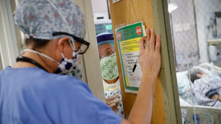 Una enfermera habla con el médico residente Leslie Bottrell, a la izquierda, desde el interior de una habitación de la Unidad de Cuidados Intensivos para pedir suministros después de succionar los pulmones de un paciente con COVID-19 (AP/John Minchillo)