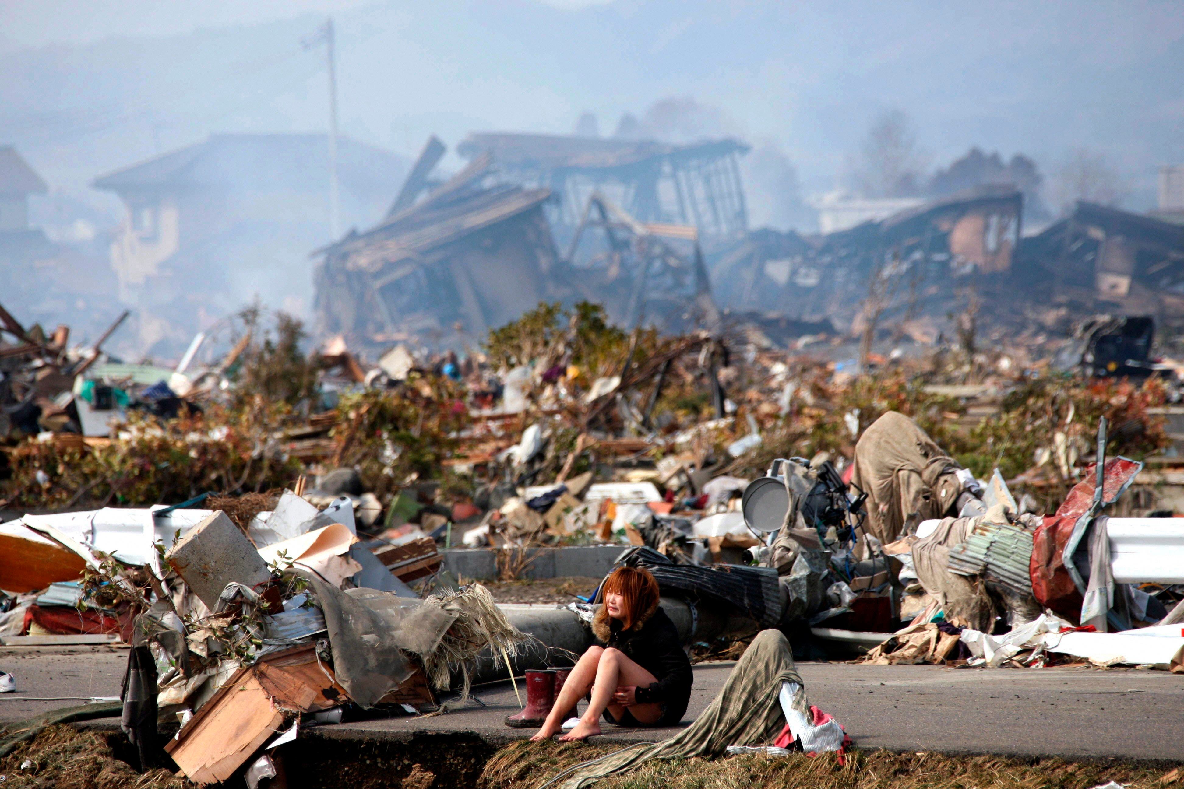 Una mujer sentada cerca de los escombros en la ciudad de Natori, Japón, tras el terremoto y posterior tsunami que afectaron al país el 11 de marzo de 2011. Ya pasaron doce años (EFE/EPA/ASAHI SHIMBUN)