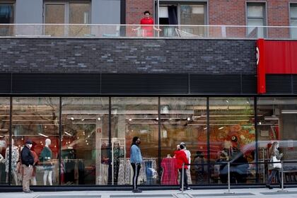 Un hombre salta soga desde su balcón, mientras clientes forman fila con distanciamiento social en una tienda de ropa (Reuters)
