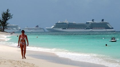 Una mujer camina a lo largo de la playa Seven Mile con tres cruceros anclados en el puerto de George Town, Islas Caimán, cuando la pandemia por coronavirus aún permitía el turismo en las islas (Reuters)