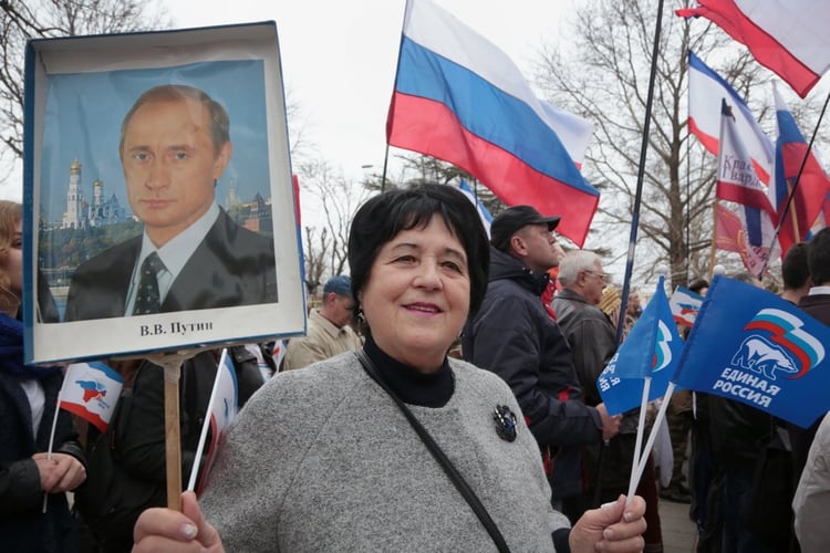 Una mujer que sostiene un retrato del presidente ruso Vladimir Putin participa en una manifestación que conmemora el tercer aniversario de la votación de Crimea para abandonar Ucrania y unirse al estado ruso en el centro de Simferopol el 16 de marzo de 2017. / AFP PHOTO / Max Vetrov