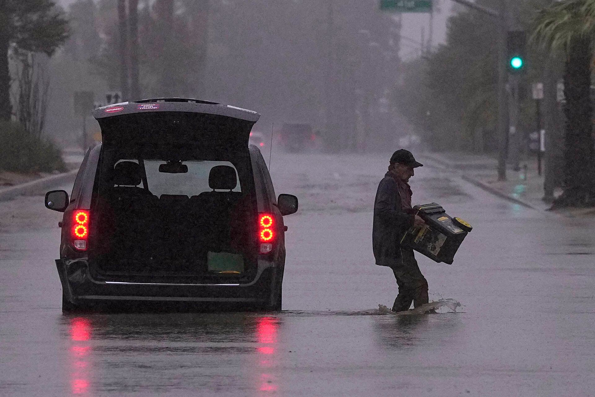Un automovilista saca pertenencias de su vehículo después de quedar atrapado en una calle inundada, en Palm Desert, California.