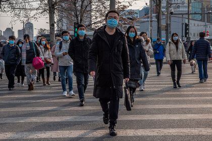 Personas que se protegen con mascarillas con máscaras protectoras cruzan por un paso de cebra en el distrito financiero de Pekín, China. EFE/EPA/ROMAN PILIPEY 