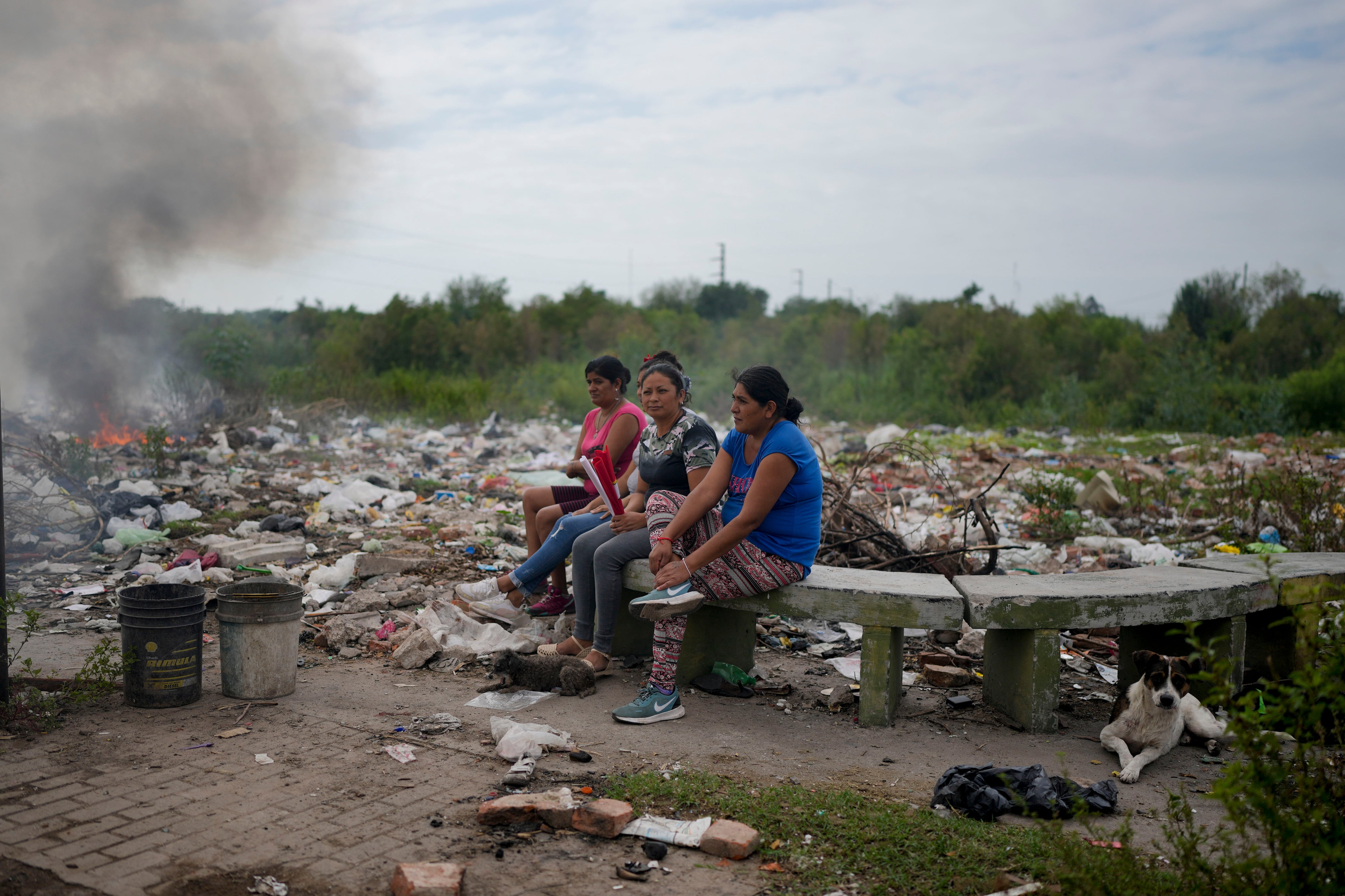 Mujeres se sientan en un banco en un predio donde se tira la basura, cerca de sus casas, en Tucumán (AP Foto/Natacha Pisarenko)