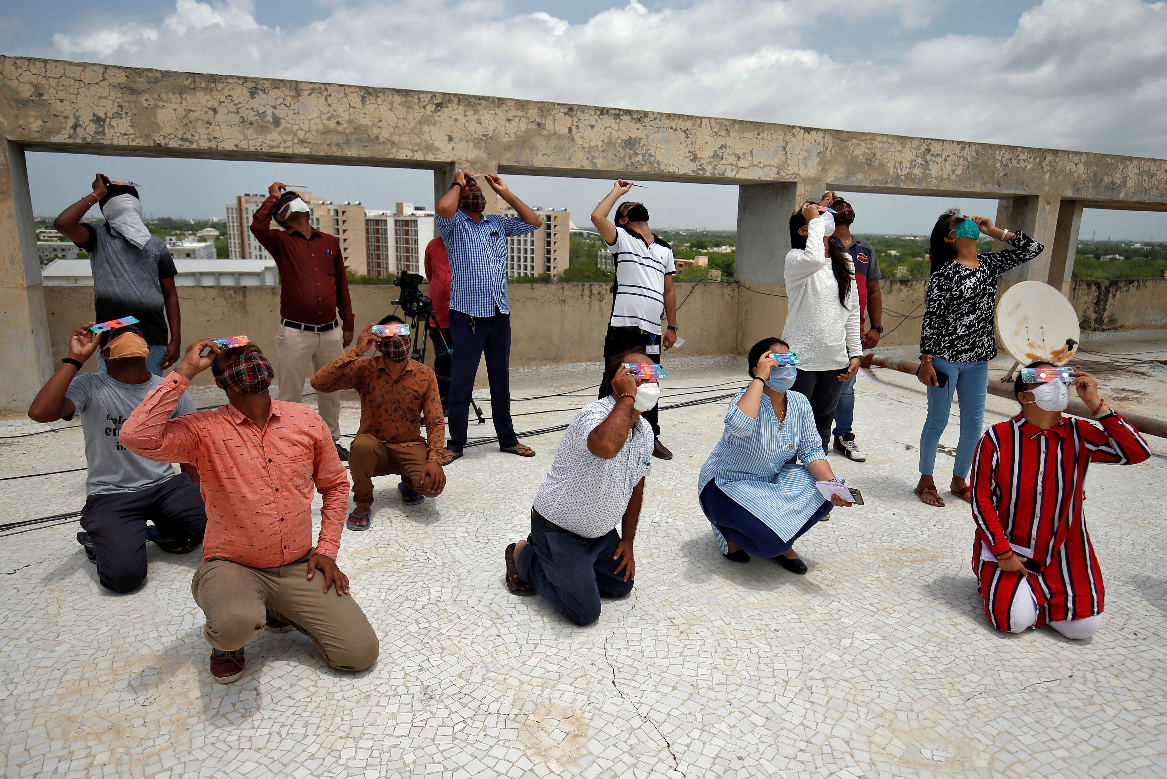 People, wearing protective face masks against the coronavirus disease (COVID-19) outbreak, use solar viewers to watch a partial solar eclipse at Gandhinagar, India, June 21, 2020. REUTERS/Amit Dave