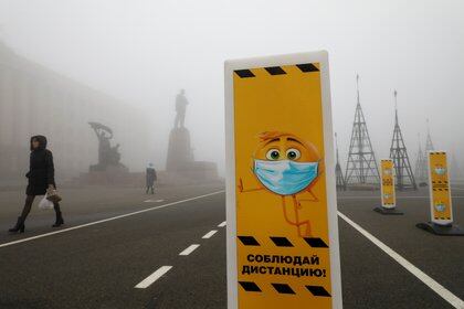 Pedestrians walk near a skating rink past signs requesting to wear protective face masks and to keep a social distance amid the coronavirus disease (COVID 19) outbreak, as heavy fog covers a square named after Soviet state founder Vladimir Lenin in Stavropol, Russia December 1, 2020. REUTERS/Eduard Korniyenko