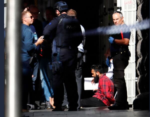 Uno de los detenidos, el supuesto conductor del vehículo, esposado y custodiado. (Herald Sun)