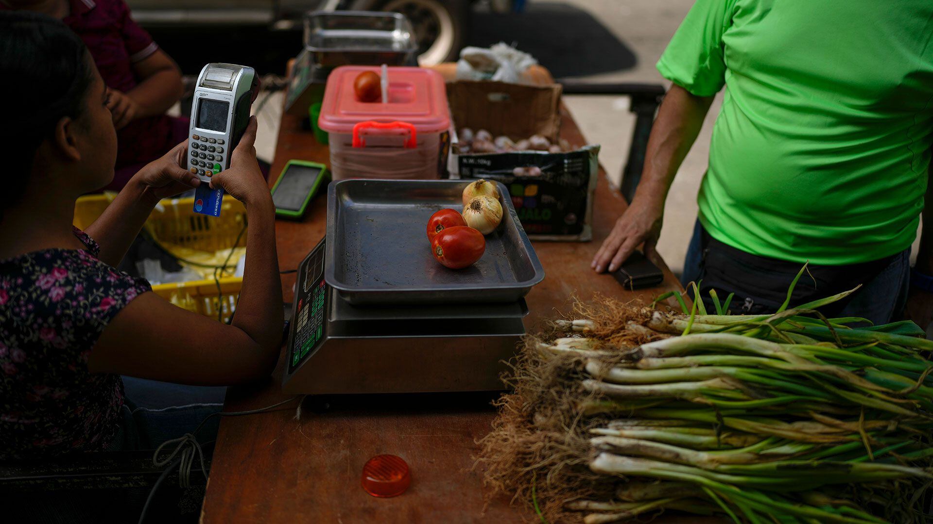 Una vendedora usa una terminal de pago para cobrarle a un cliente su compra de tomates y cebollas, en Caracas (AP Foto/Ariana Cubillos)