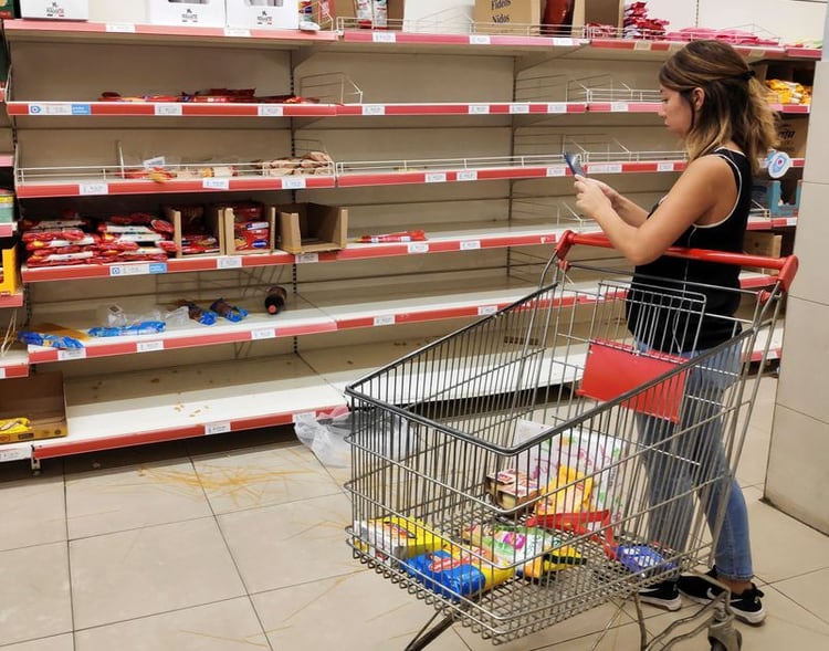 Una mujer toma una foto de fideos desparramados en el piso frente a estantes de pasta vacíos en un supermercado, mientras la gente acudía a comprar comida por el brote de coronavirus, en Buenos Aires, Argentina, el 15 de marzo de 2020 (REUTERS/Agustin Marcarian)