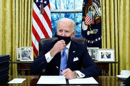 Joe Biden se ajusta su máscara facial mientras firma órdenes ejecutivas y habla con periodistas en la Oficina Oval de la Casa Blanca en su primer día como presidente de EEUU (REUTERS/Tom Brenner)