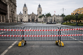 Rejas metálicas con cintas rojas y blancas bloquean una calle vacía en el Centro Histórico de Lima, con la Catedral y la Plaza Mayor visibles al fondo bajo un cielo gris.