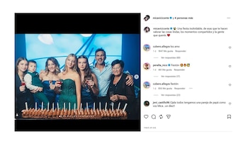 Micaela Viciconte y Fabián Cubero de pie con cinco niños y una mujer mayor, todos sonriendo, frente a una torta con velas y un fondo azul iluminado