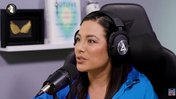 Natalia Salas con camisa azul y audífonos negros habla frente a un micrófono en un estudio de pódcast