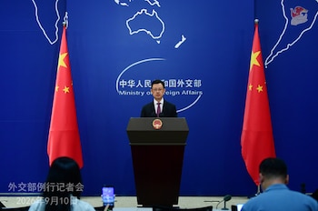 Guo Jiakun de pie detrás de un podio con el escudo chino, flanqueado por dos banderas de China y con un telón azul al fondo