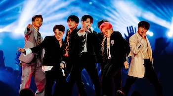 Los integrantes del grupo musical BTS posan en un escenario con fondo de luces azules y siluetas de espectadores.