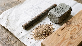 Una varilla de acero, un bloque de concreto, un puñado de arena y una tabla de madera sobre un plano arquitectónico.