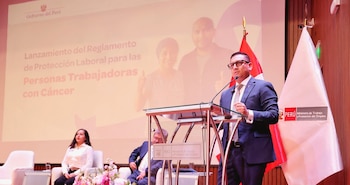 Hombre con traje en podio con micrófono. Pantalla con texto "Lanzamiento del Reglamento de Protección Laboral". Banderas de Perú y logo Ministerio de Trabajo. Mujer sentada