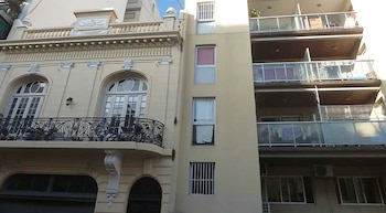 Fachada de dos edificios contiguos. A la izquierda, uno clásico y ornamentado en crema con balcón de hierro. A la derecha, uno moderno beige con balcones de vidrio