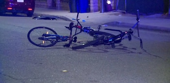 Una bicicleta dañada sobre el pavimento de una calle nocturna, con restos de piezas alrededor y un vehículo al fondo