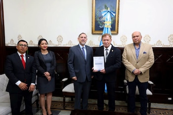 Personas ordenando folios sobre una mesa larga frente a cajas amarillas numeradas con textos impresos