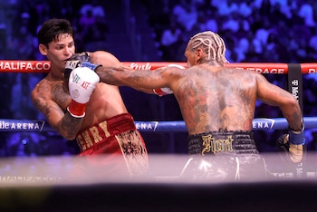 Dos boxeadores combaten dentro de un cuadrilátero delimitado por cuerdas ante la presencia de público en la tribuna