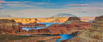 Vista aérea del Lago Powell con aguas azules rodeado por formaciones rocosas de arenisca en tonos naranjas y rojos bajo un cielo azul con nubes dispersas