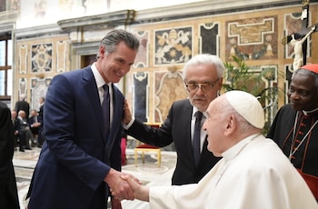 Gavin Newsom estrecha la mano del papa Francisco en una sala decorada con mármol y un crucifijo