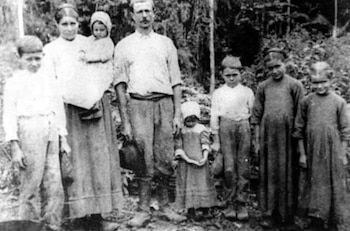 Fotografía en blanco y negro de una familia numerosa de colonos, con padres y seis hijos, posando al aire libre en un entorno con vegetación densa