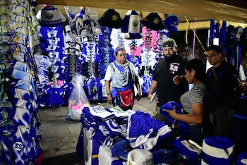 Cuatro personas en un puesto repleto de camisetas, gorras y sombreros de color azul y blanco con símbolos de El Salvador