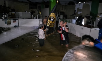 Oficina inundada con agua que cubre el piso. Varias personas, una con una bandera negra y otra con un teléfono en la oreja, están de pie en el agua