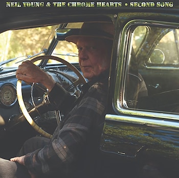 Neil Young con sombrero y camisa a cuadros sentado al volante de un automóvil clásico negro y mirando por la ventana