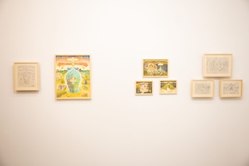 Pared blanca con nueve obras de arte enmarcadas: una pintura grande, cuatro pinturas pequeñas y cuatro dibujos, todos con marcos de madera claros