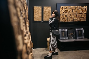 Una mujer con ropa oscura y falda a rayas observa cuadros de relieve en madera colgados en una pared negra