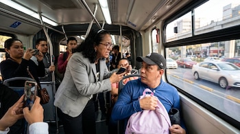 Interior de Metrobús con una mujer de pie señalando a un hombre sentado con mochila lila, mientras otros pasajeros graban la escena con sus teléfonos.