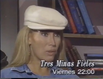 Mujer rubia con gorra beige y camisa azul de mezclilla. Estantería con libros en el fondo. Texto superpuesto: Tres Minas Fieles, Viernes 22:00