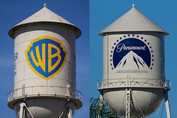 Dos torres de agua. Una con logo amarillo y azul 'WB'. Otra con logo azul 'Paramount' con montaña y estrellas. Fondo de cielo azul