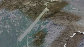 Fotografía aérea de una pista de aterrizaje gris sobre un paisaje de roca, hielo y caminos de acceso
