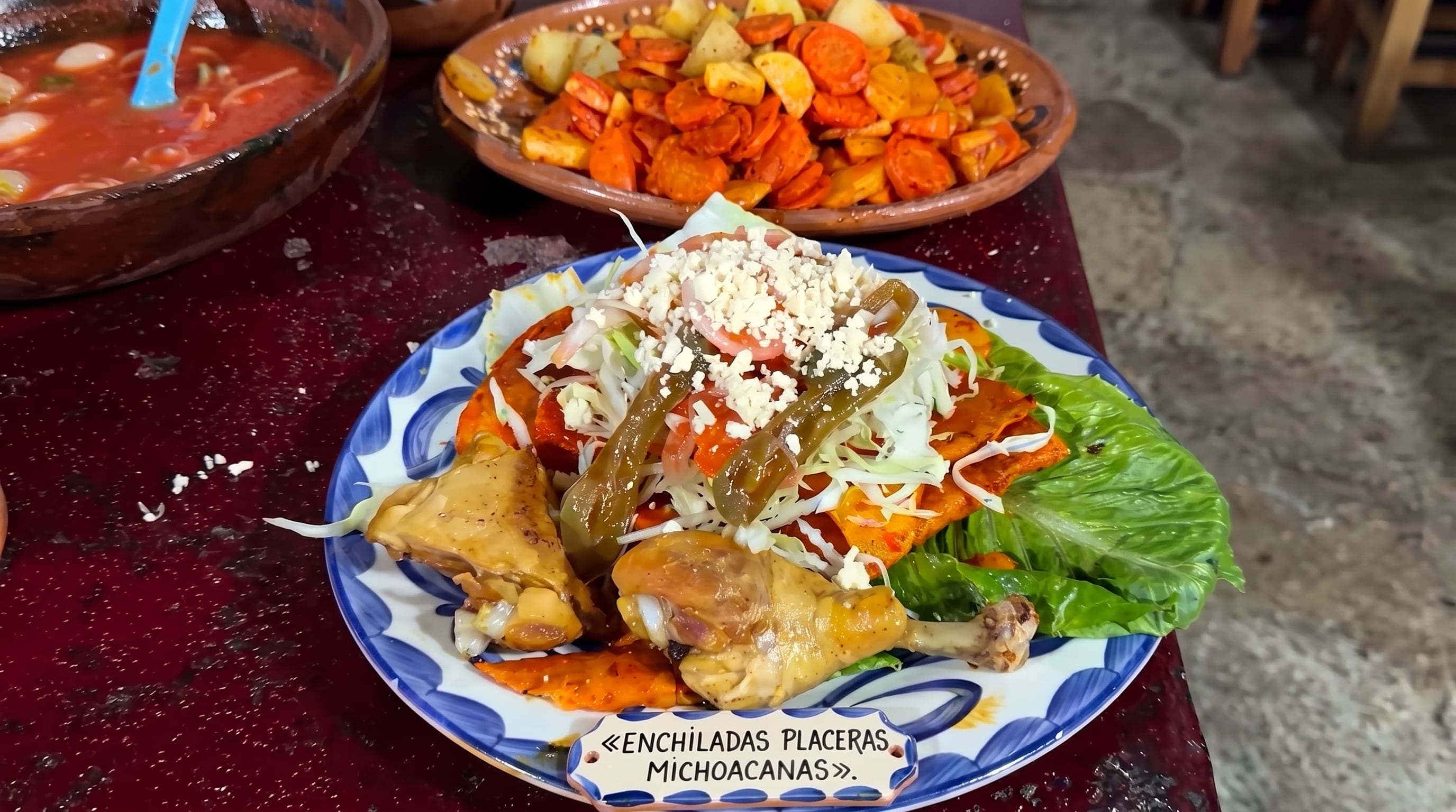 Un plato tradicional de enchiladas placeras michoacanas se presenta acompañado de piezas de pollo, lechuga, queso y chiles, junto a guarniciones de verduras en recipientes de barro. (Imagen Ilustrativa Infobae)