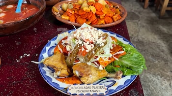 Un plato con enchiladas, piezas de pollo, queso rallado y chiles, con una etiqueta que dice enchiladas placeras michoacanas.
