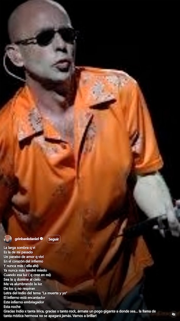 Daniel Grinbank, un hombre calvo con gafas de sol oscuras y camisa naranja estampada, sosteniendo un micrófono, sobre un fondo oscuro