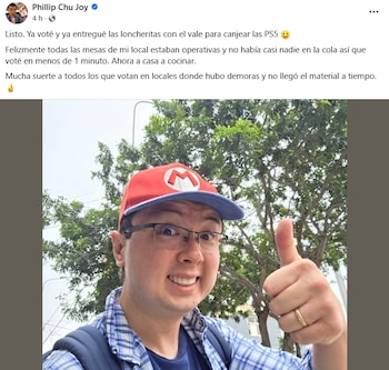 Phillip Chu Joy sonríe y muestra un pulgar hacia arriba, lleva una gorra roja y azul de Mario Bros, gafas y una camisa a cuadros. El fondo es verde con árboles